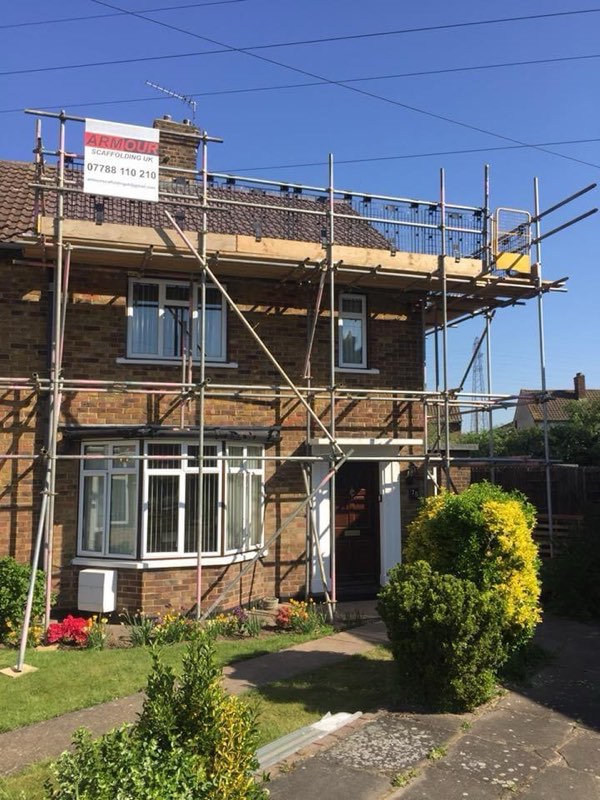 Semi-detached brick house with scaffold at eaves height and an Armour Scaffolding board