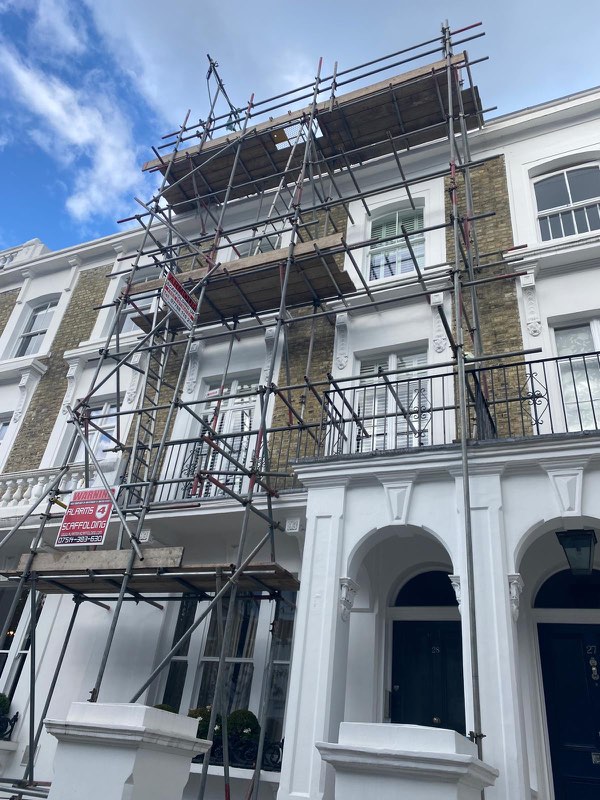 Four-storey white stucco townhouse with scaffold climbing to the roofline