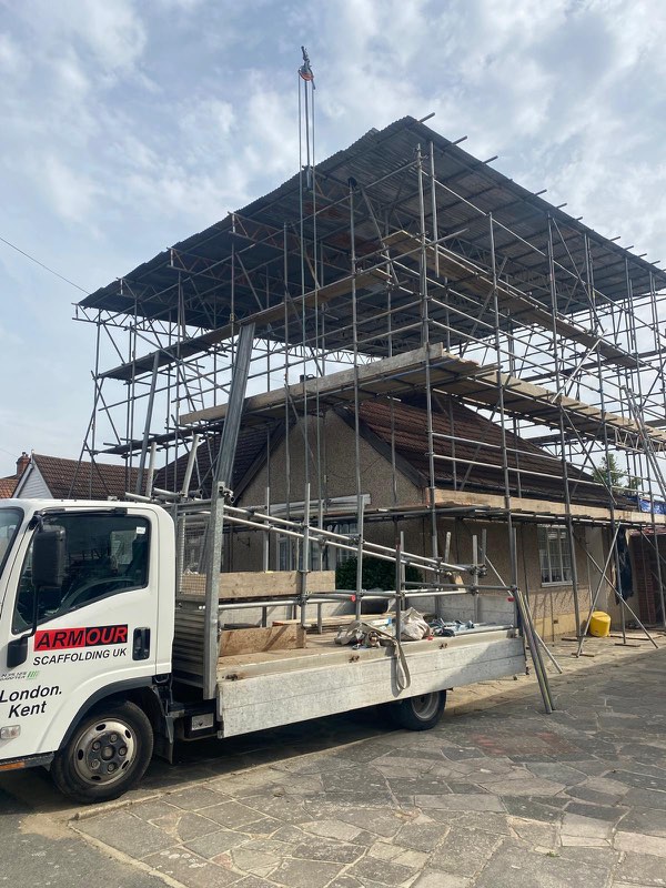 Full scaffold tower rising above a house roof with an Armour Scaffolding lorry parked in front