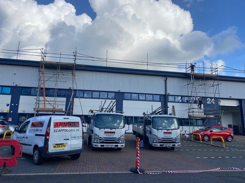 Armour van and two lorries parked in front of an industrial unit with scaffold on the front elevation