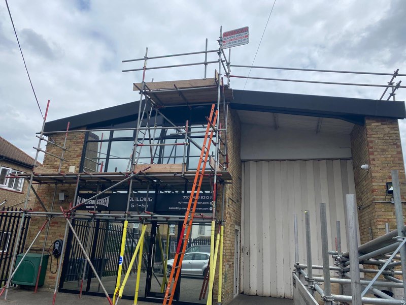 Two-storey commercial building with scaffold, orange ladder access and yellow guard posts