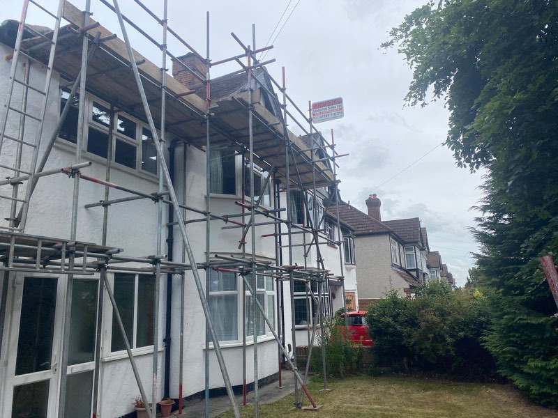 Scaffold on the side of a house with a tree-lined road behind