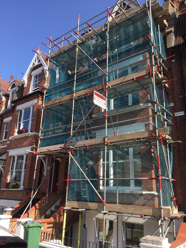 Red-brick Victorian house covered in netted scaffold with ladder access